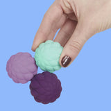 A hand holding three connected, petal-textured magnetic fidget spheres on a solid blue background.