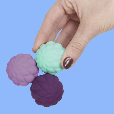 A hand holding three connected, petal-textured magnetic fidget spheres on a solid blue background.