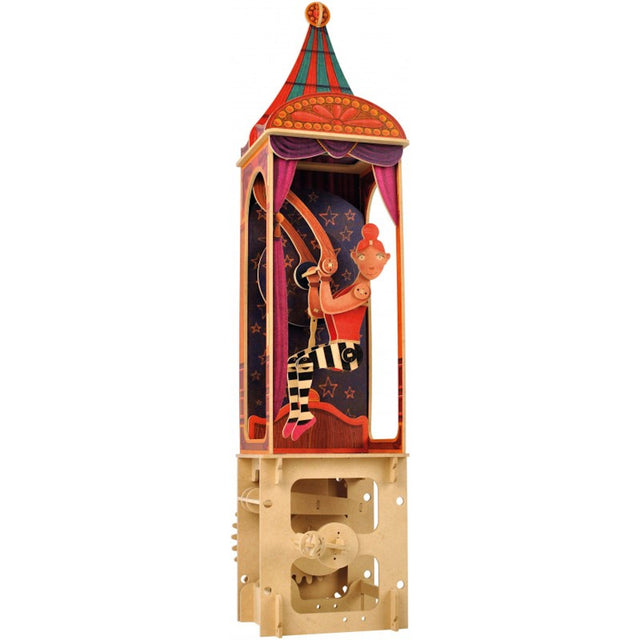 A colorful paper automaton of a circus performer with orange hair on a trapeze, encased in a vibrant, star-patterned tower. The base reveals gears.