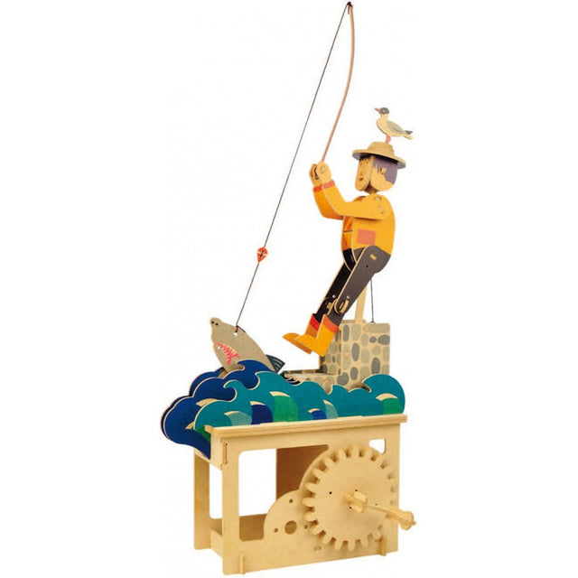 Wooden automaton of a fisherman on a rock fishing for a shark in colorful waves, with a seagull on his hat. Hand crank visible below. Playful and whimsical.