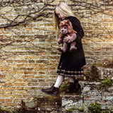 Young girl in a coat holding a brown plush monster toy while stepping down stone stairs near a brick wall.