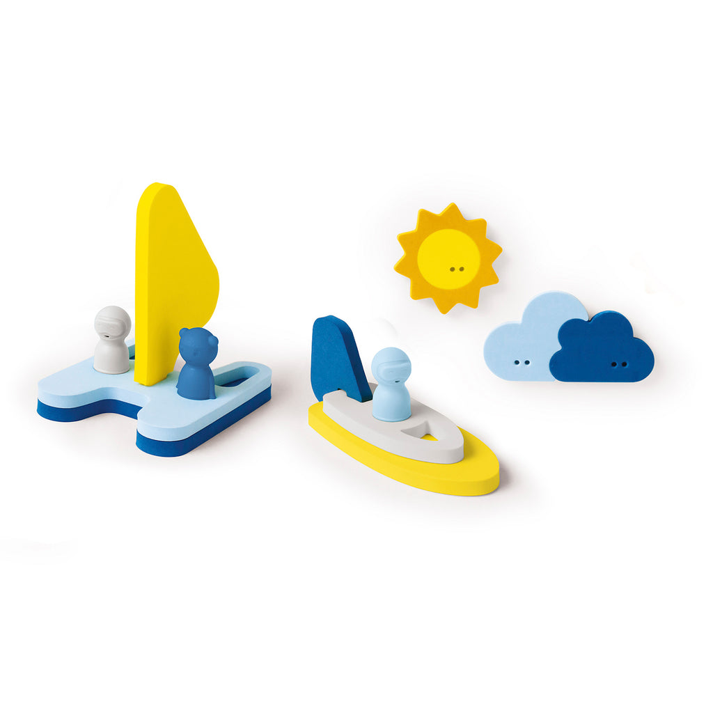 Toy sailboats and figures are arranged with a yellow sun and blue clouds, creating a playful, nautical scene. Bright colors convey a cheerful mood.