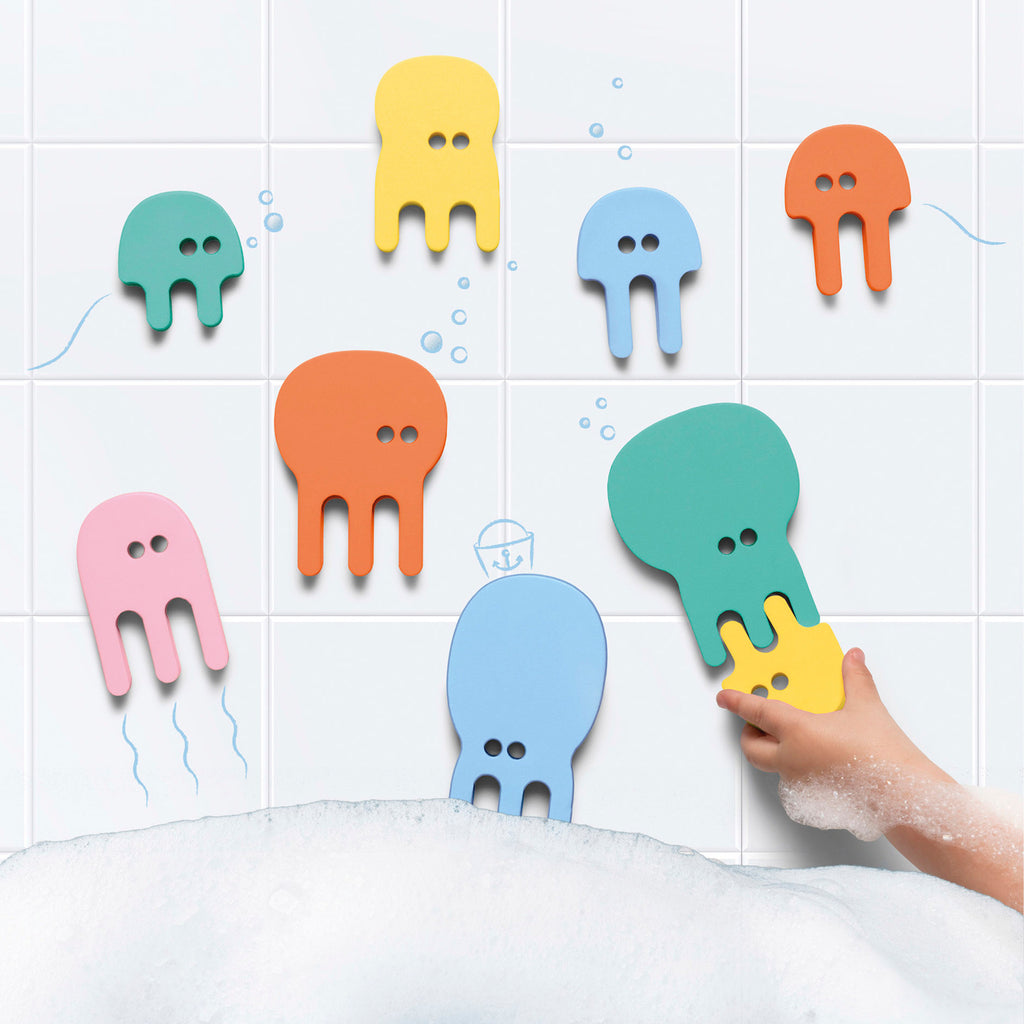 Playful bath scene with colorful, cartoon-like jellyfish shapes stuck on white tiled wall. Child's hand plays, surrounded by foam bubbles. Fun, whimsical vibe.