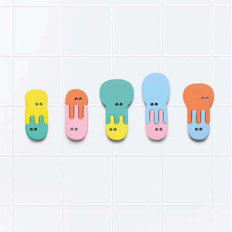 Five colorful, interlocking foam jellyfish bath toys stuck in a row on a white tiled wall.