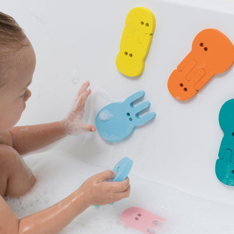 Toddler playing with colorful foam jellyfish puzzle bath toys sticking to a white bathtub wall.