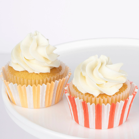 Two cupcakes with swirled white frosting in orange and red striped liners on a white plate.