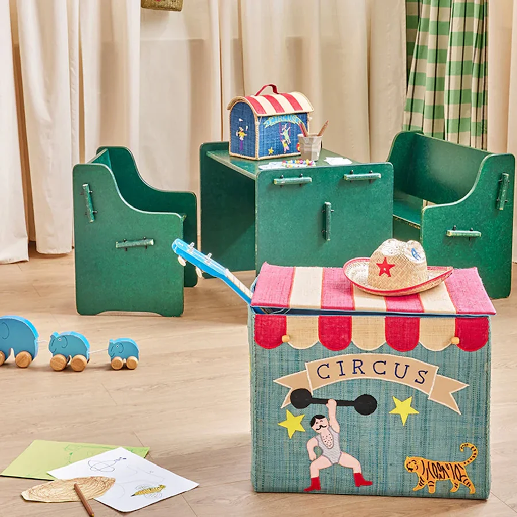 Children's playroom with circus-themed decor. A colorful toy chest, green chairs and table, toy elephants, and drawings create a whimsical, playful atmosphere.