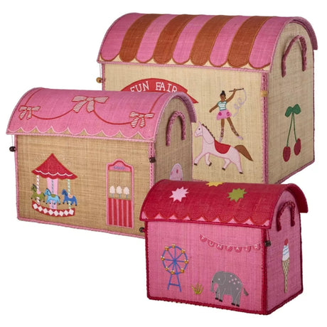Three woven raffia toy baskets shaped like fun-fair houses in varying sizes, featuring pink roofs and circus motifs.