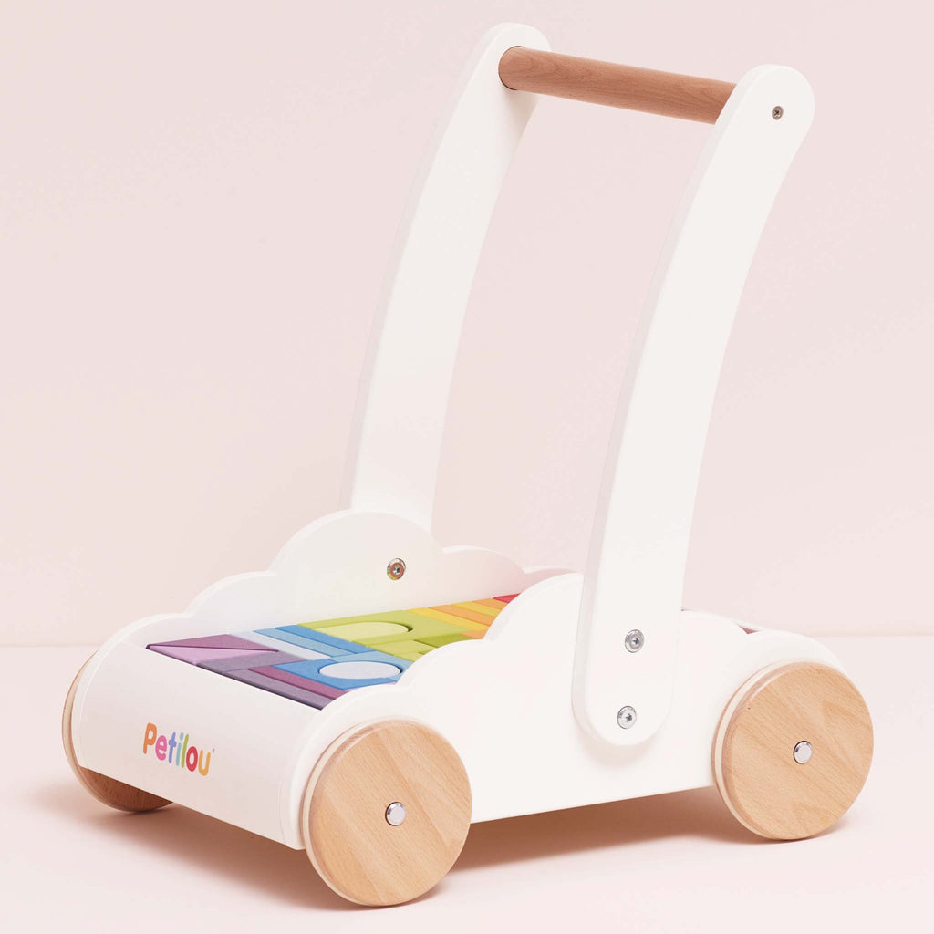 Wooden baby walker with a white frame, natural wood wheels, and rainbow-colored blocks. The design is playful and cute, set against a light pink background.