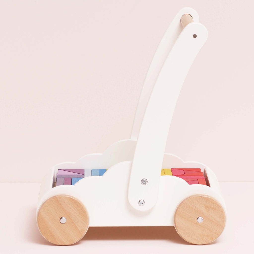 Wooden baby walker with a white frame, natural wood wheels, and rainbow-colored blocks. The design is playful and cute, set against a light pink background.