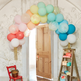 Large rainbow balloon arch with gold tassels displayed over a wooden doorway in a decorated party setting.