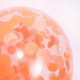 Close-up of a clear party balloon filled with round orange tissue paper confetti dots.