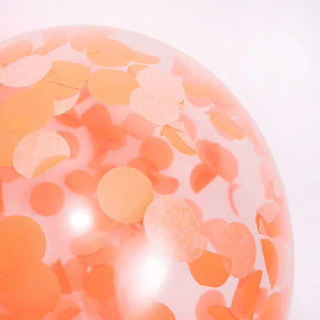 Close-up of a clear party balloon filled with round orange tissue paper confetti dots.
