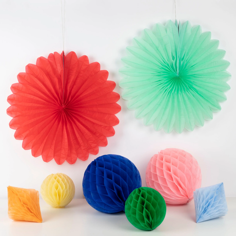 Hanging red and mint green paper fans with colorful honeycomb balls and diamonds on a surface below.