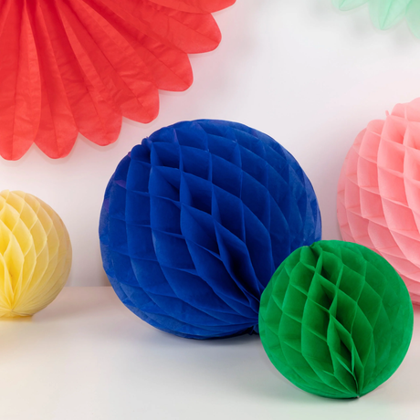 Close-up of vibrant blue, green, yellow, and pink paper honeycomb party decorations against a white wall.