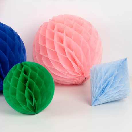 Close-up of pink, blue, and green paper honeycomb decorations resting on a white surface.