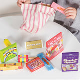 A child placing wooden toy candy into a pink striped bag with play sweets set on a table.