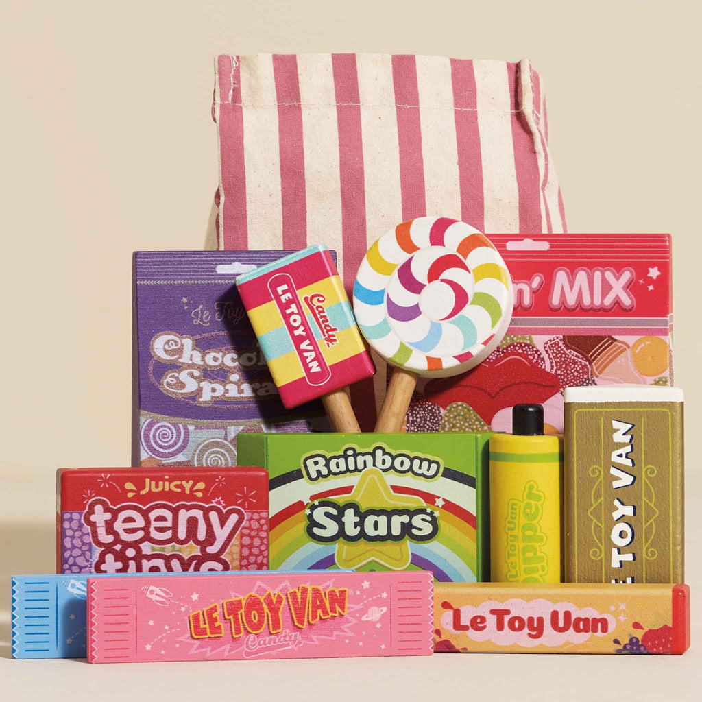 A vibrant assortment of colorful toy candies with labels like "Le Toy Van" and "Rainbow Stars," displayed in front of a red and white striped bag. Playful and cheerful atmosphere.
