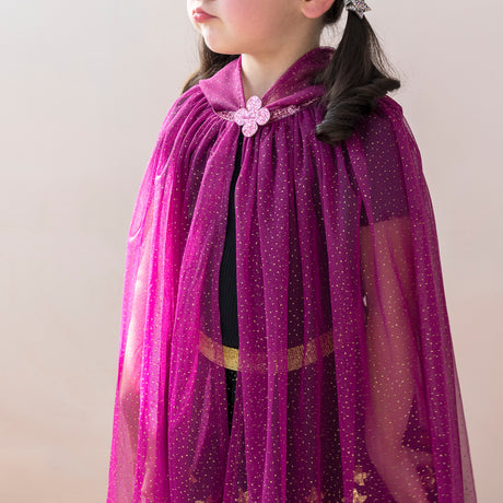 A young girl wears a magenta, sparkly cape with a flower brooch. Her hair is styled in pigtails, conveying a whimsical, playful tone.