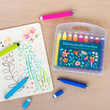 A colorful set of 18 felt tip pens labeled "Fairies in the Garden" sits beside an open sketchbook filled with doodles of flowers and a butterfly. A vibrant and creative atmosphere is conveyed.