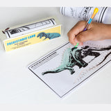 Child's hand coloring a dinosaur dot-to-dot page with a multicolor pen. Nearby is a "Prehistoric Land" coloring set box. The scene feels playful and creative.