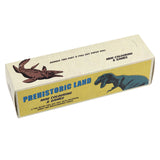 Box for "Prehistoric Land Mini Colouring & Games," showcasing dinosaur illustrations. Features a yellow and beige design with text and retro artwork.