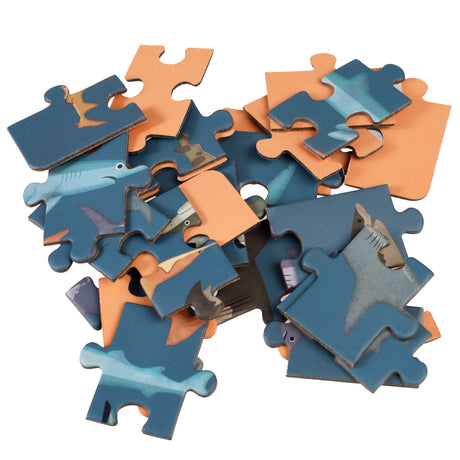 Scattered blue and orange shark jigsaw puzzle pieces on a white background for a Rex London mini 24-piece kids' puzzle.