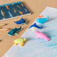 Toy sea animals, including a turtle, whale, dolphin, and seal, are arranged on a desk with colored pencils and a shark-patterned notebook. Playful vibe.