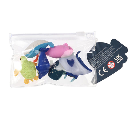 A clear plastic bag contains colorful toy sea animals, a green turtle, blue whale, pink seal, and manta ray. A warning and CE mark is visible on a tag.