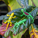 Three colorful toy lizards in yellow, green, and multicolored sit on a large, textured leaf with shades of green and brown, evoking a playful mood.