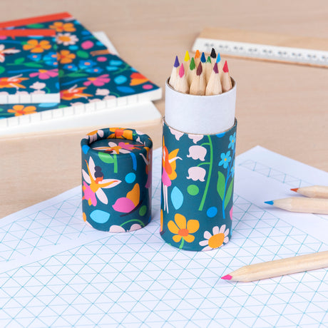 Colorful pencils in a floral tube sit on grid paper with more floral stationery and wooden ruler, creating a vibrant, creative workspace ambiance.