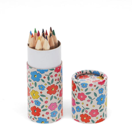 A round floral-patterned case holds pointed colored pencils, with the lid off beside it. The colorful flowers create a cheerful and artistic feel.