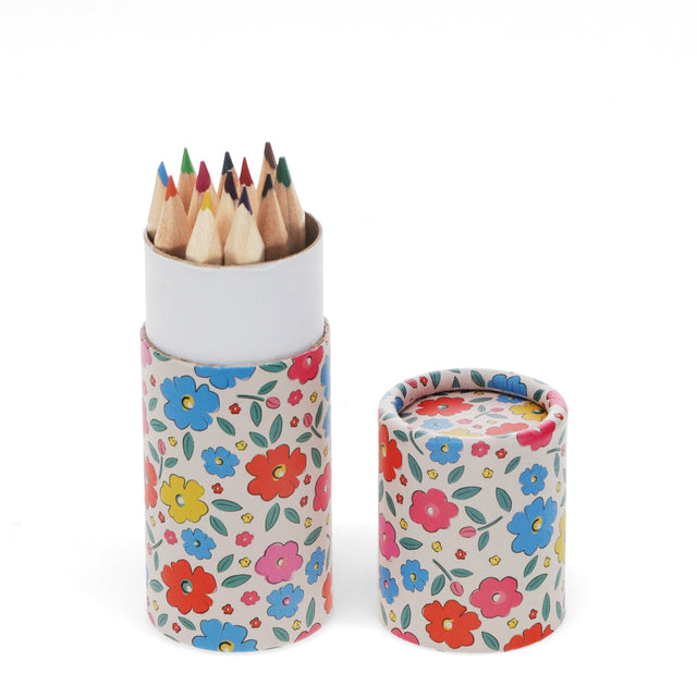 A round floral-patterned case holds pointed colored pencils, with the lid off beside it. The colorful flowers create a cheerful and artistic feel.
