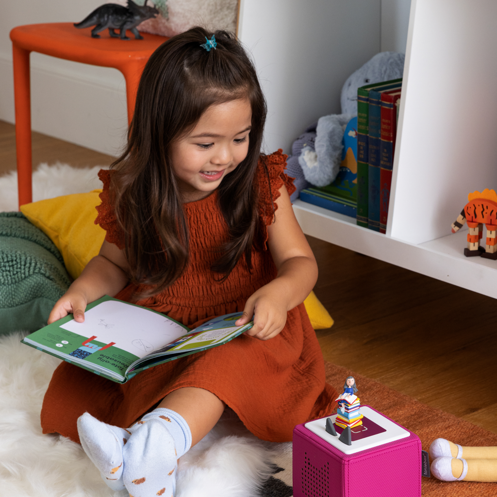 A whimsical figurine sits atop a colorful stack of books, evoking a playful reading theme.