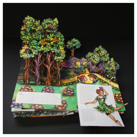 Pop-up book depicting a vibrant fairy-tale scene with colorful trees, a stone archway, and a small path. A fairy figure appears animated and whimsical.