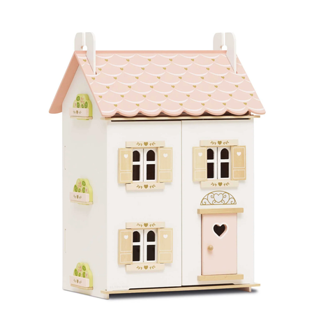 Wooden dollhouse with a pink scalloped roof and white walls. Features windows with tan shutters, heart details, and a pink door, creating a charming, cozy feel.