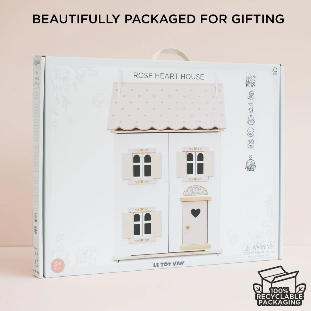 Packaging for a toy dollhouse called "Rose Heart House." Features a pink roof with gold hearts, windows, and a door. Labeled "Beautifully packaged for gifting" and "100% recyclable packaging."