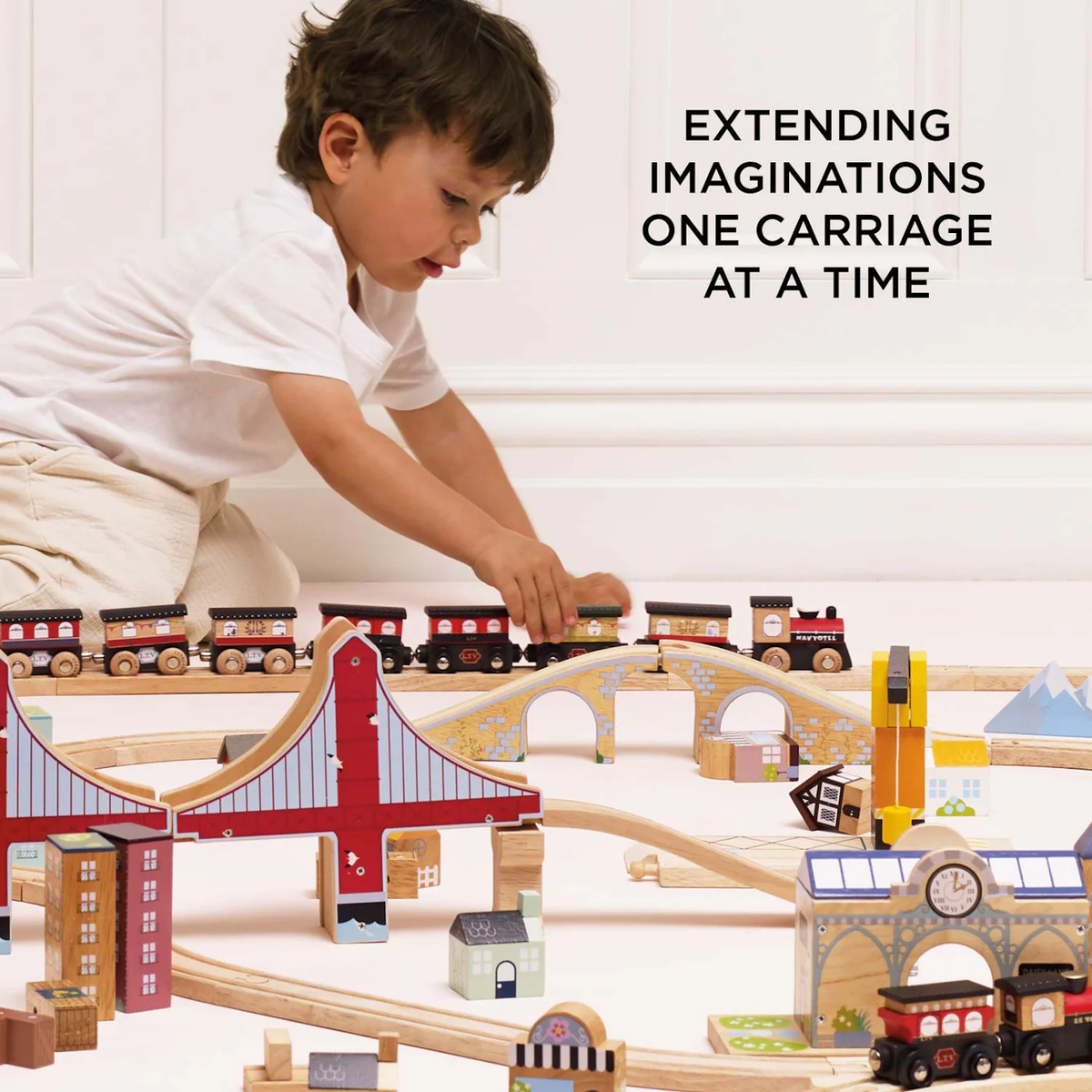 A child plays with a wooden train set featuring bridges and buildings, conveying a sense of creativity and exploration. Accompanied by the text, "Extending imaginations one carriage at a time."