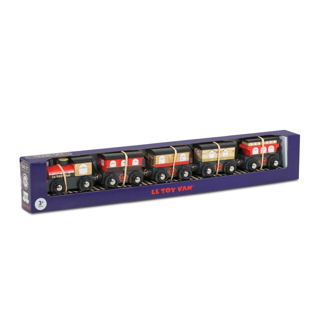 A boxed wooden toy train set features a red and black engine with four matching cars. The packaging is navy blue with "Le Toy Van" in red.
