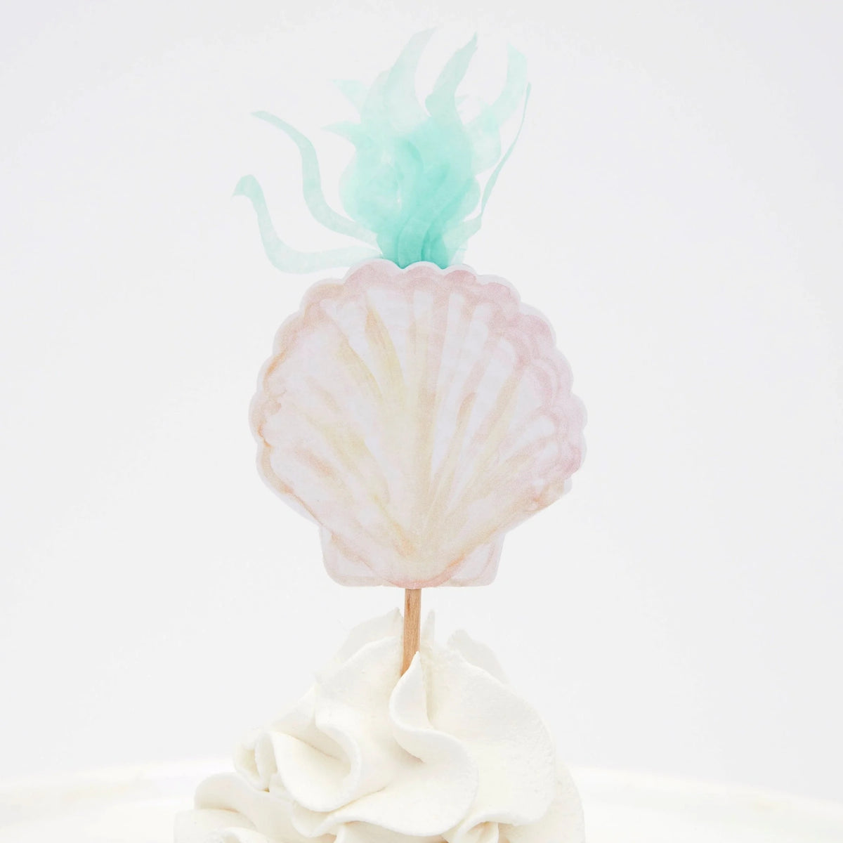 A seashell-shaped topper with green seaweed details on top of a frosted white cupcake.