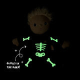 Plush doll in a skeleton costume with glowing green embroidered bones against a dark background.