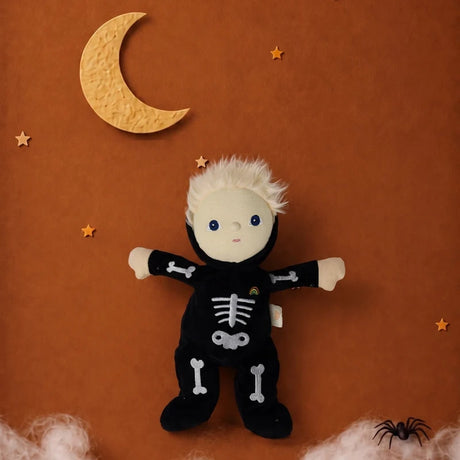 Skeleton plush doll set against a brown backdrop with a crescent moon, stars, cobwebs, and a spider.