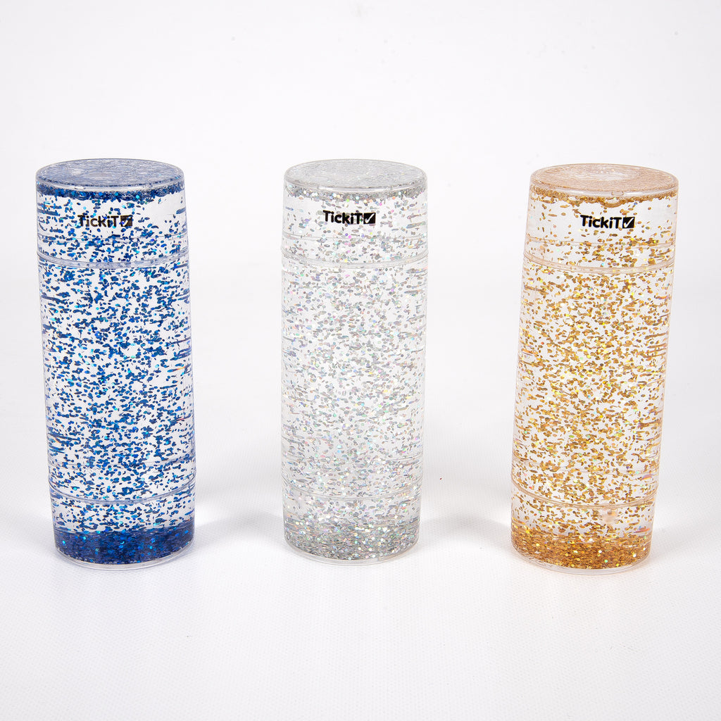 Three tall, clear cylinders filled with blue, silver, and gold glitter, set against a white background. Each has a black logo near the top.