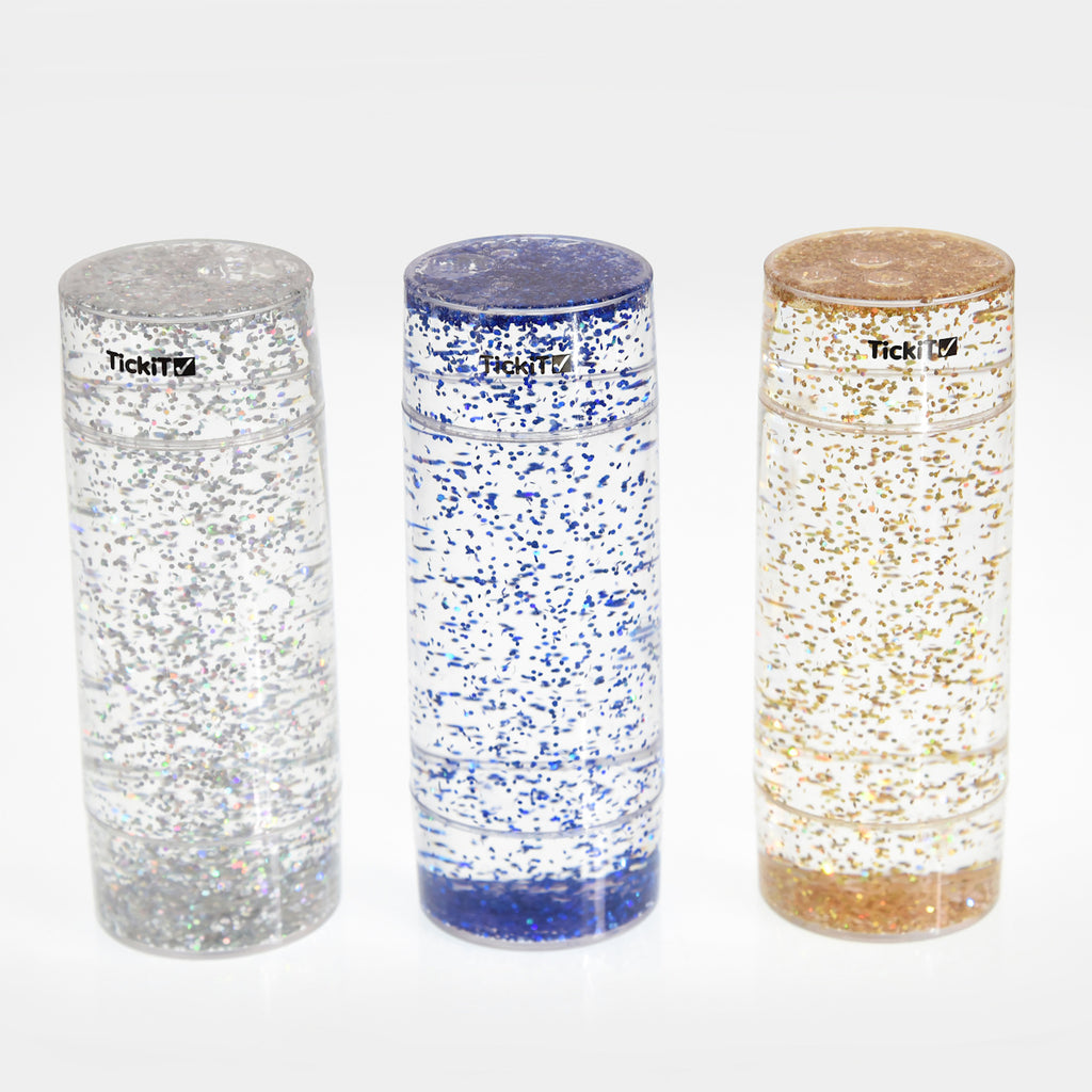 Three tall, clear cylinders filled with blue, silver, and gold glitter, set against a white background. Each has a black logo near the top.