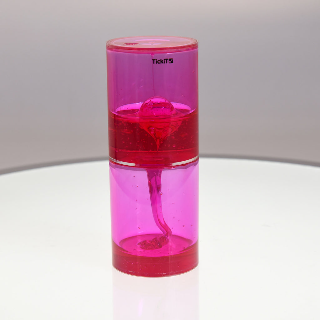 Pink liquid motion timer with bubbles inside a transparent cylindrical container, placed on a white surface, creating a calming, playful vibe.