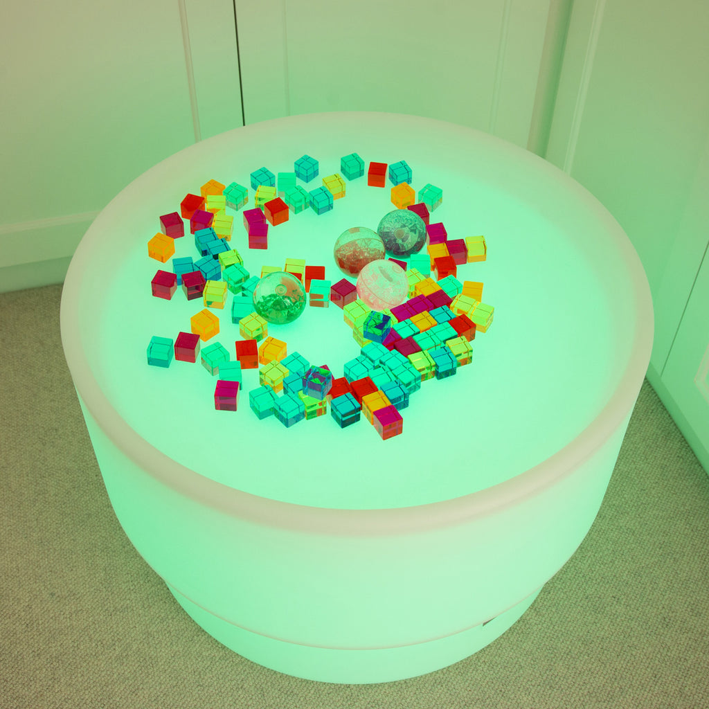 A round table bathed in vibrant green light, scattered with colorful toy blocks and several textured balls. The scene is playful and surreal.