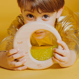 A child dressed in gold holding the Petit Boum Flow Moon sensory toy, engaging with its glittery, crescent-shaped sensory window.