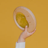 A small hand lifting the Petit Boum Flow Moon sensory toy against a yellow background, showing off the dreamy crescent moon design.