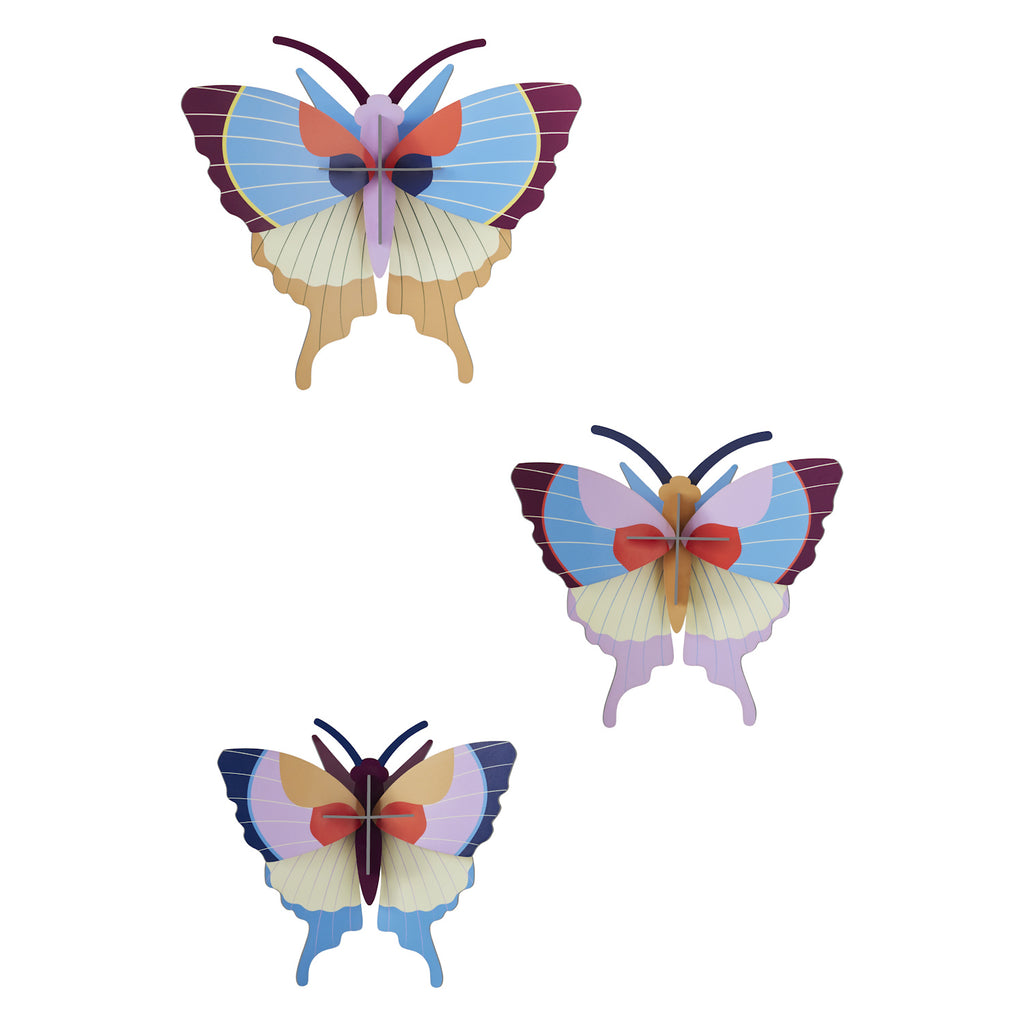 Three colorful, stylized butterfly wall decorations with layered wings in shades of blue, purple, and red, creating a whimsical and artistic tone.