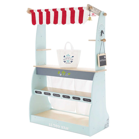 Wooden market stand toy with striped awning, shelves, fabric shopping bag, and an "Open" sign.